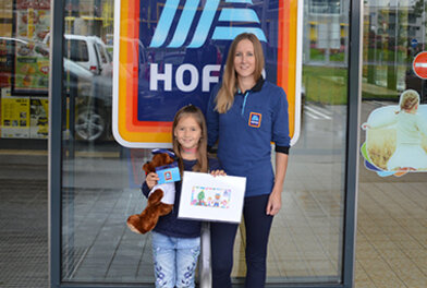Gewinnerin des HOFER Malwettbewerbs vor Filiale bei Gewinnübergabe mit ihrer Mama.