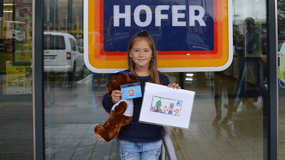 Gewinnerin des HOFER Malwettbewerbs vor Filiale bei Gewinnübergabe.