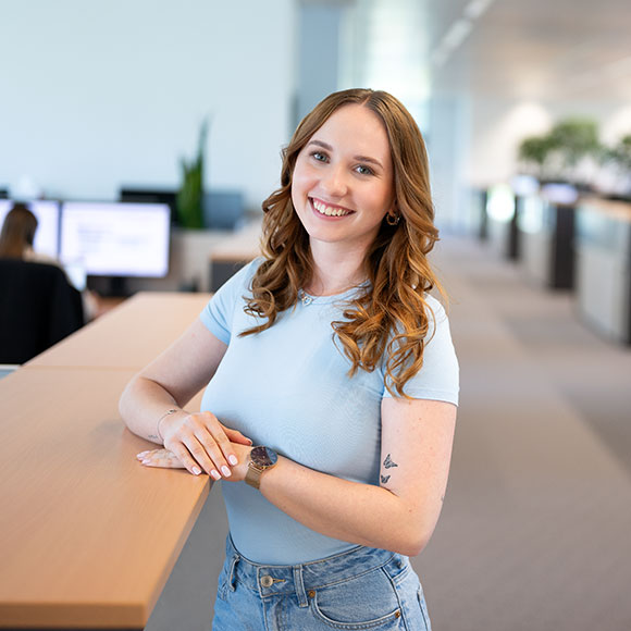 Mitarbeiterin steht bei ihrem Arbeitsplatz am Schreibtisch mit Bildschirm