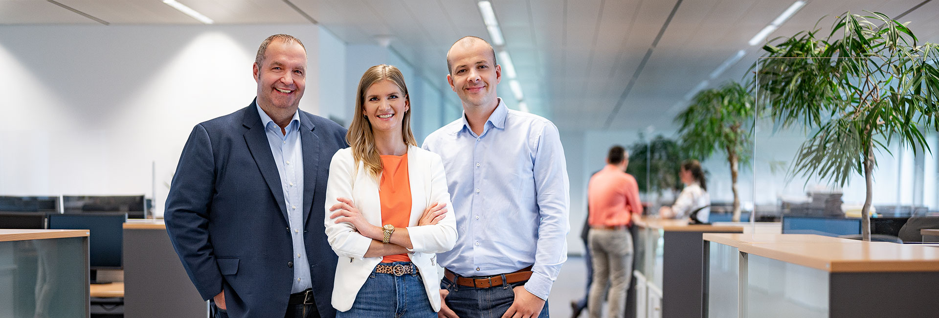 Mitarbeitergruppe aus drei Personen stehend im Büro mit Blick Richtung Kamera