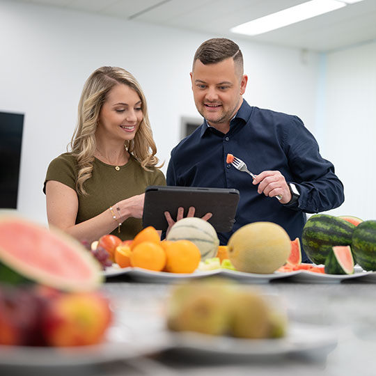 zwei Mitarbeiter protokollieren Ergebnisse einer Verkostung von Obst in einem Tablet
